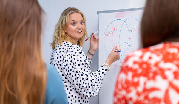 Clinician atwhiteboard presenting to two women in the foreground