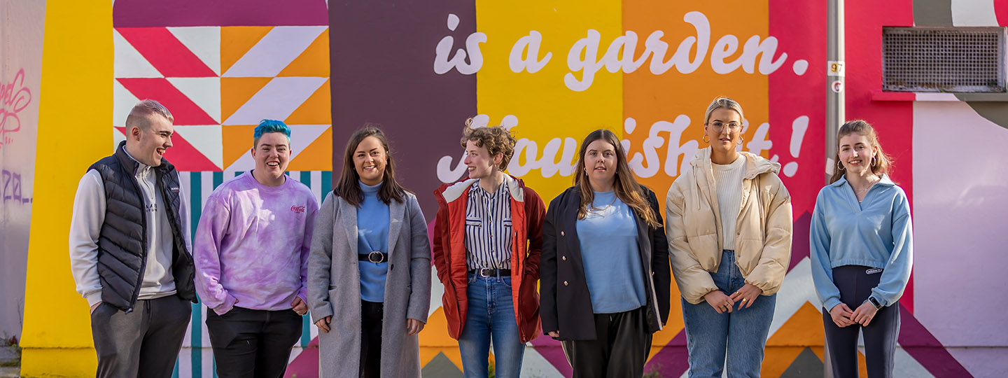 line up of young people in front of a coloured mural
