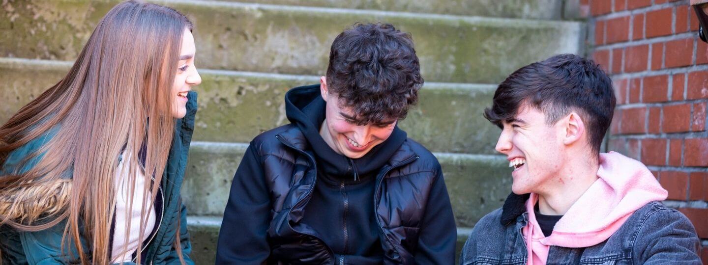 Two young people, girl and boy sitting down laughing on a grey couch
