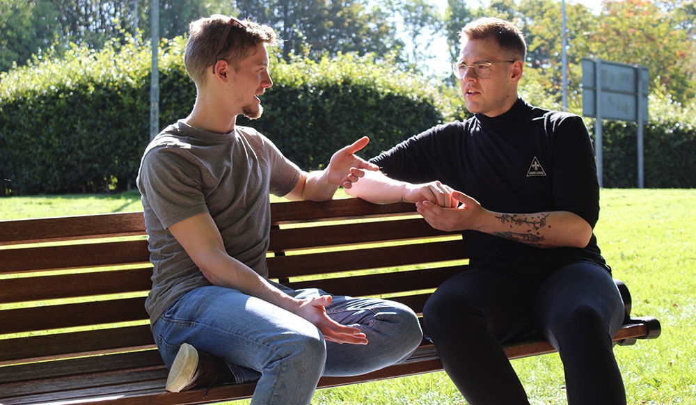 Two young men chatting in the park Two-young-men-chatting-on-a-park-bench