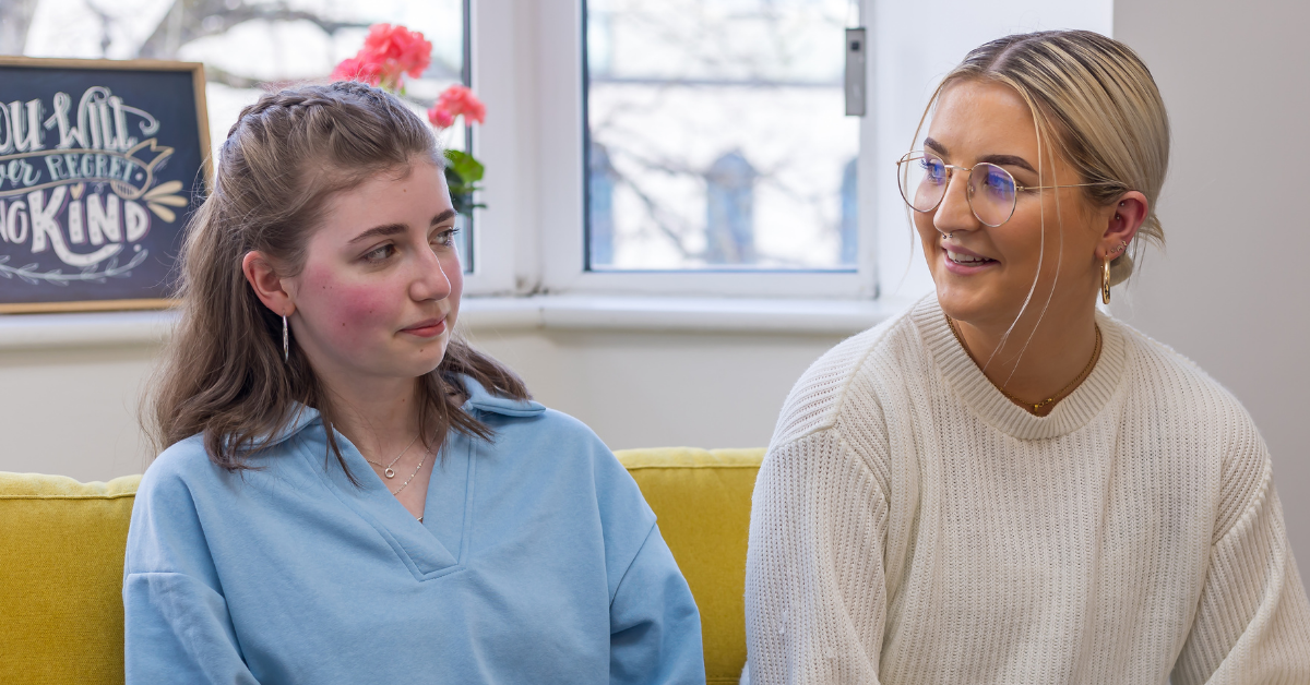 2 young women sitting on yellow couch