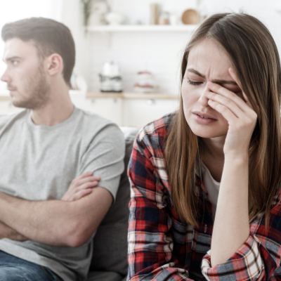 Picture of young woman holding a hnad to her head with a young man in the background