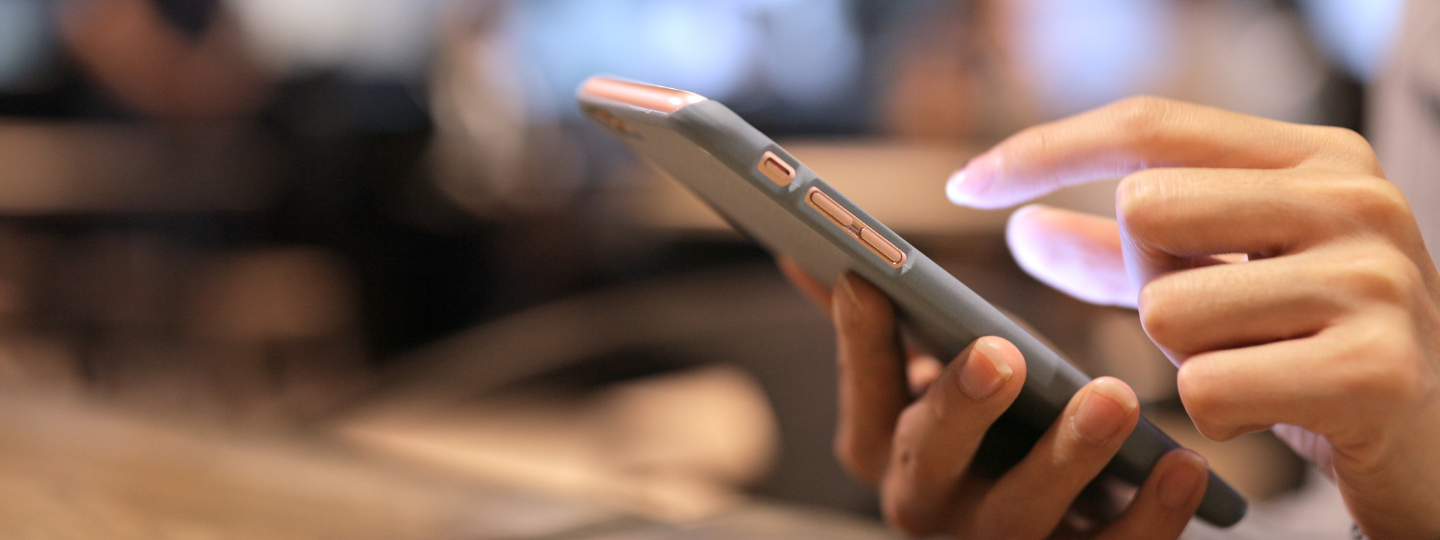 Image of a pink phone in a girls hand. The background features a café