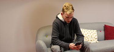 Picture of a young man sitting down looking at his phone